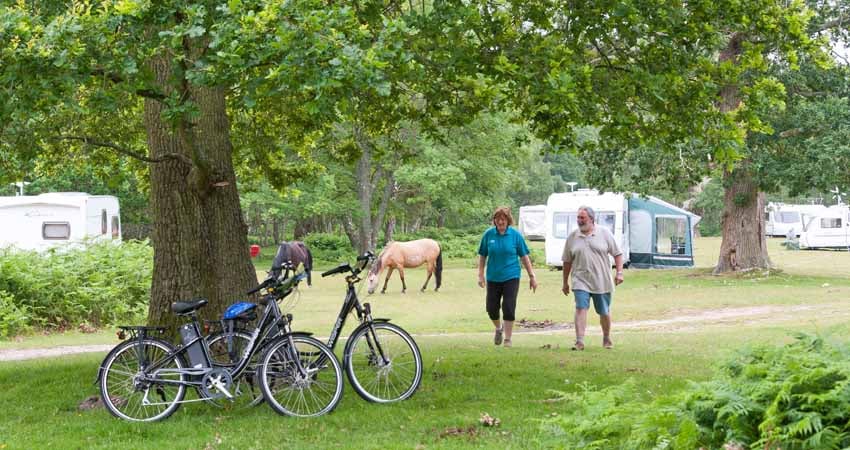 Two people walking to their bikes at Denny Wood campsite in the New Forest.