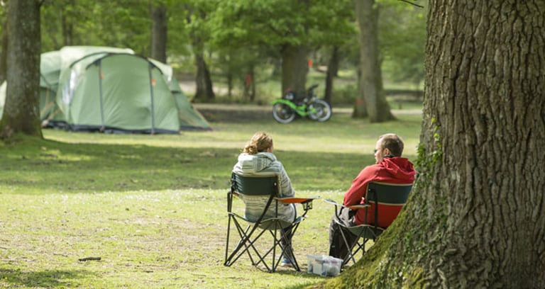 Two people sat in chairs at Hollands Wood campsite in the New Forest.