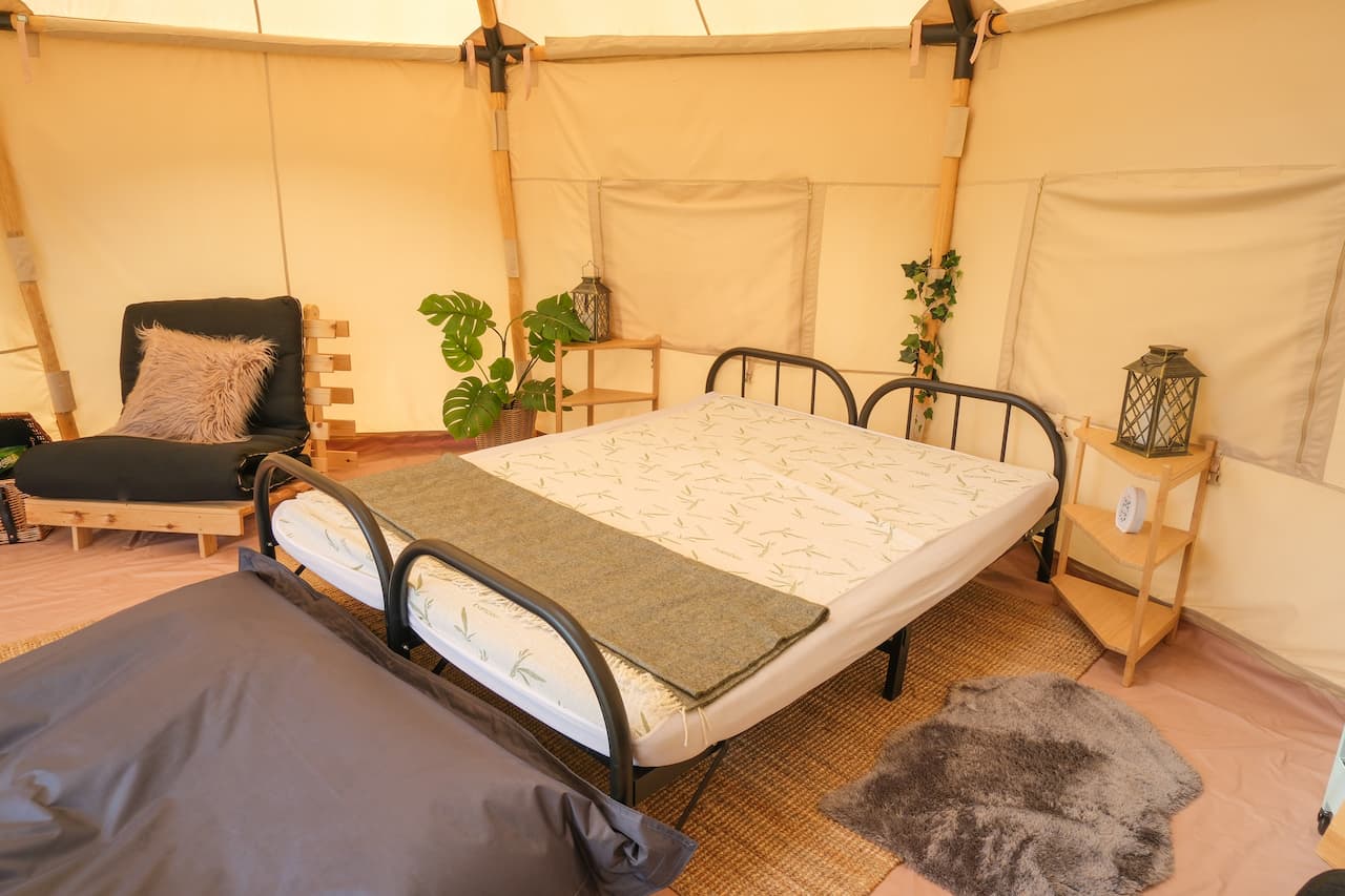 Interior of a furnished glamping bell tent with double bed and seating at Long Meadow