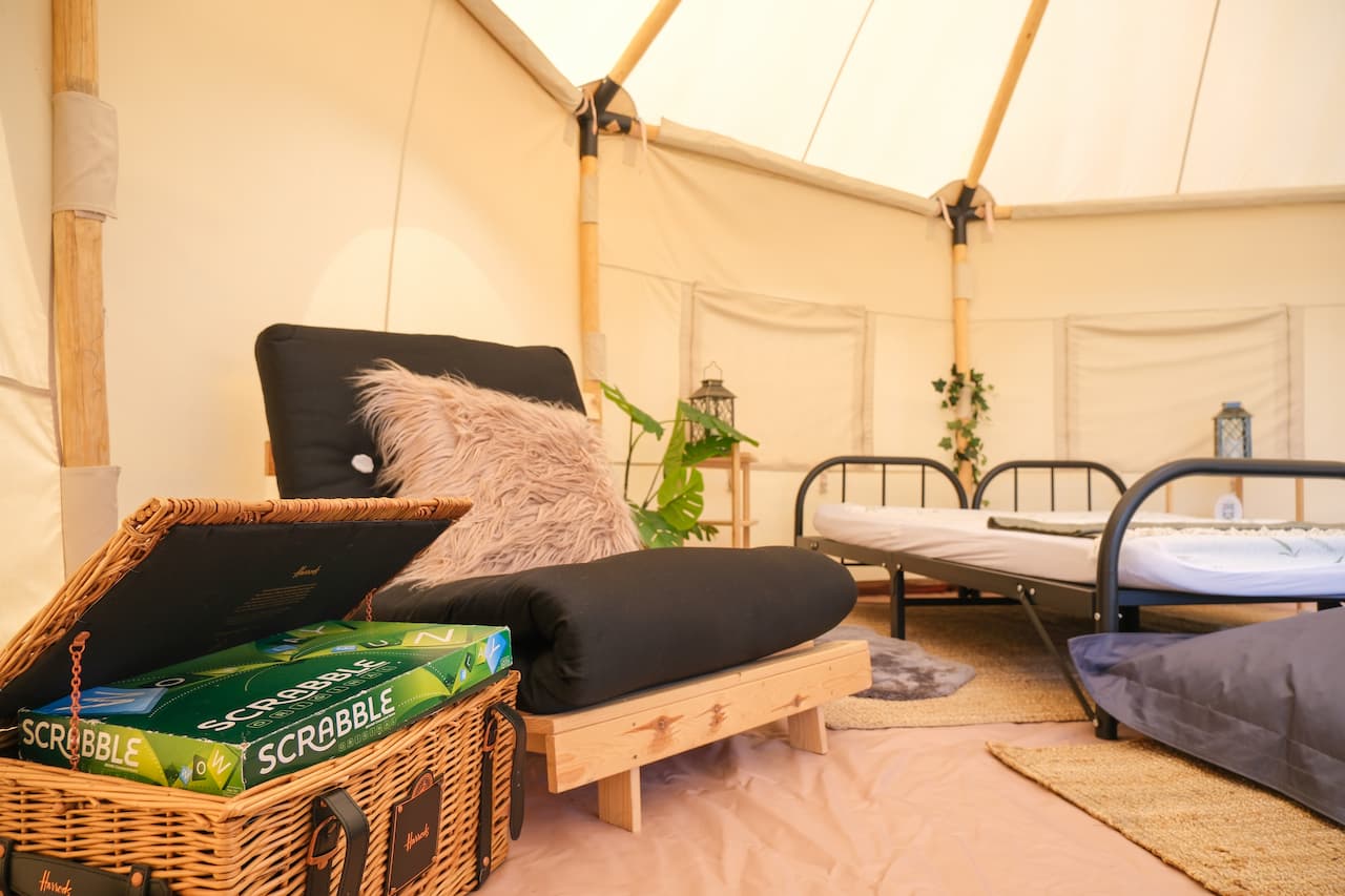 Interior of a bell tent with seating area, beds and board games at Long Meadow
